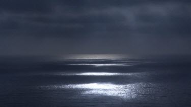 Full moon over ocean, through gap in clouds