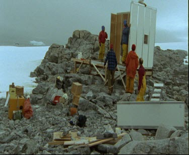 Men assembling new prefabricated hut in Australian Antarctic.  Cape Denison Commonwelath Bay on rocky promontory.