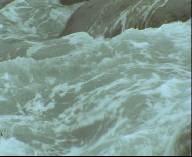 Topshot Adelie penguins swimming in rough waters. High surf, waves crashing penguin comes out onto rocks.