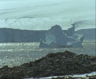 Thick white ice shelf. Water glistening, reflection of sunlight on ice and water.