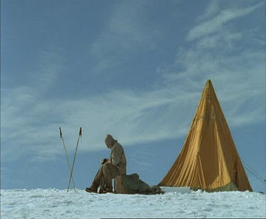 One man camping in snowy white landscape Medium shot. He is reading or writing