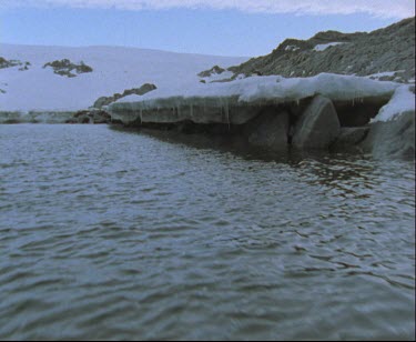 Bay with overhanging ice sheet or ice shelf. Mawson's hut in background.