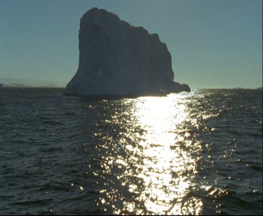 Silhouette backlit iceberg with bright sunshine in background.