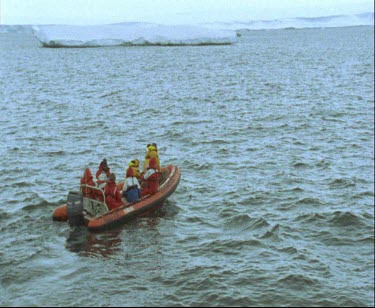 Men  aboard zodiac inflatable dinghy  setting off for land. Ice sheet ice shelf in background.