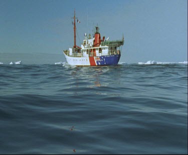 Ice-breaker ship with Australian flag painted on its side. Icebergs and icefloes in background