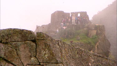 One of the highest parts of Machu Picchu with tourists exploring inside with lots of mist