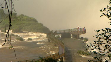 Tourist on a walkway over Iguaz Falls panning back to a wide shot