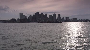 Boston skyline. To boats in the distance. Bird flying from left to right, small motorboat going from right to left in the distance.