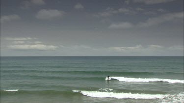 Surfer comes into beach on gentle wave.