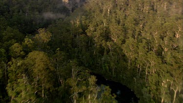 Aerial over deep river valley. River meandering meanders. Small wispy clouds hang over the valley