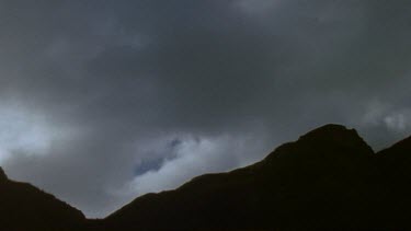 Clouds blowing over the top of silhouetted mountain