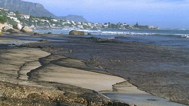 Oil washes up onto beach. Thick layer of oil on sea.