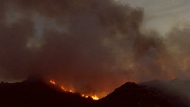 Helicopter in silhouette flies over raging fire