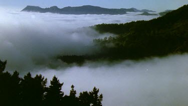 Mountain peaks stick out above low lying cloud. Wind blowing clouds.