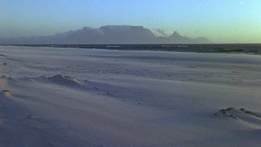 Wind blows sand along beach. Table Mountain in bg.