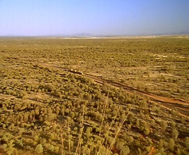 Zoom in high angle on petrol tanker driving along outback road. In the Outback all produce is moved by truck. These huge rigs are called road trains. This petrol tanker is more than 53 metres long.