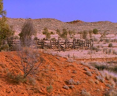 Cattle truck driving up hill creating dust. Skull of animal. Broken fences and dry red earth of desert beyond.