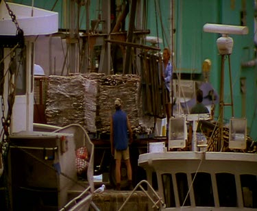 Small commercial fishing boats docked in harbour port. Lots of seagulls flying around. Fishermen loading bait onto boats.