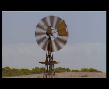 Windmills blowing in the wind. WS sheep in very dry dusty environment gathering to drink beneath the windmill