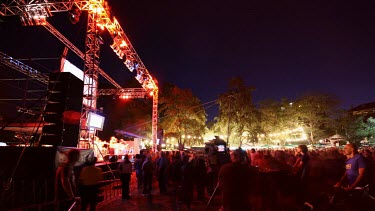 Flickers of stage lights splash into the lens at a big outdoor concert. Dramatic coloured lights.