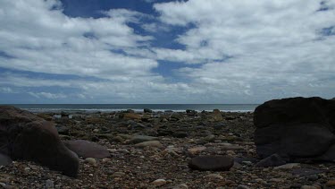 The sunlight shifts across this beach littered with rocks as the clouds pass overhead in this motion control timelapse.