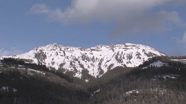 Snow covered mountain, blue sky, clouds and forest