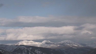 Mountain range with cloud covered snowy peaks and blue sky