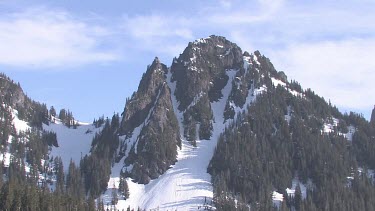 Forested snowy mountain peak with blue sky and clouds