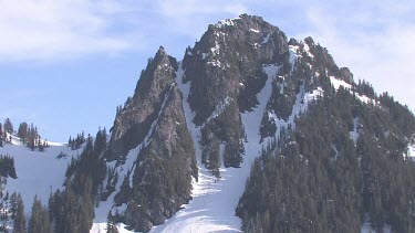 Forested snowy mountain peak with blue sky and clouds