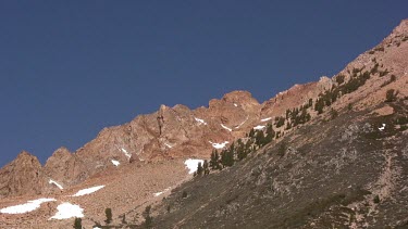 Jagged mountainside with scattered trees and blue sky