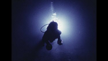 Diver swimming at night through cave in spotlight