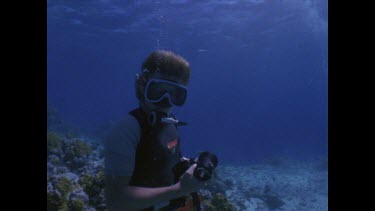 Zoom to Divers with cameras around coral table.