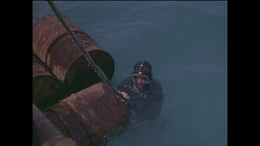 diver hangs on to rusted drums