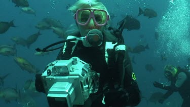 Valerie Taylor is underwater with her camera. Valerie Taylor shows "Ascend, or I am going up" hand signal and swims up. They shooting sharks without the protection of a cage.