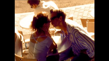 High angle. Young people at sidewalk caf kiss, pan to others with surf boards.