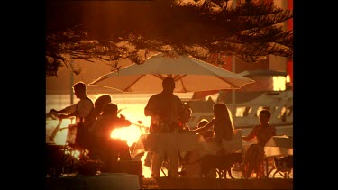 People relaxing at beachside restaurant. Yachts sail past.