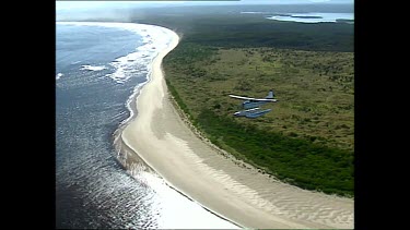 Seaplane flying over beach and sea.