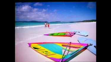 Couple jogging on beach, windsurfers lying on beach in FG. Whitsunday.