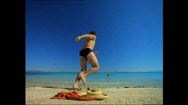 Man running into very calm, clear sea to join woman