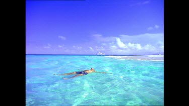 Man floating on his back in clear calm sea, yacht in background.