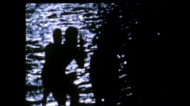 Aboriginal dancers dancing at night next to a lake or sea. Dancers in silhouette