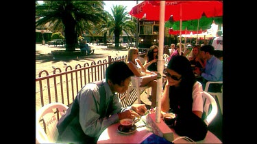 Glenelg Tram passes couple drinking coffee at sidewalk caf.