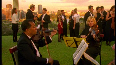 String quartet in FG, cocktail party in background. View of Perth background.