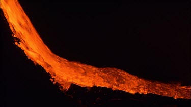 Active volcano. Lava flow. River of lava pouring down slope. Night.