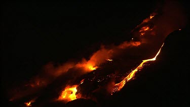 Volcano erupting. Night. The base of the volcano meets the sea. Waves crash onto the molten lava and the water steams up the side of the volcano.