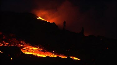 Volcano erupting. Night. People in silhouette standing on volcano watching the lava flow.