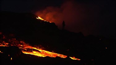 Volcano erupting. Night. People in silhouette standing on volcano watching the lava flow.