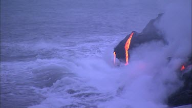 Waves crashing onto lava flow and turning into steam. Lava dropping into ocean. daybreak sunrise.