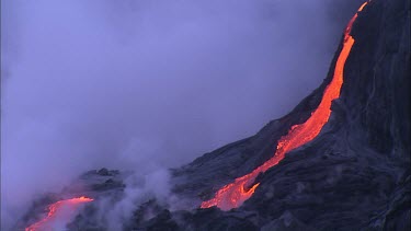 Lava flowing down channel. Steam. Recently solidified lava crust.