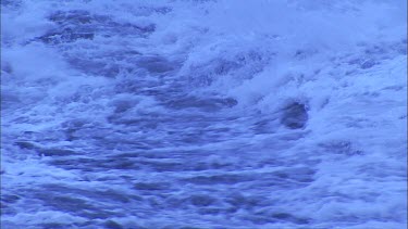 Waves steam and lava flowing into ocean. Cooled lava has solidified into black rock.